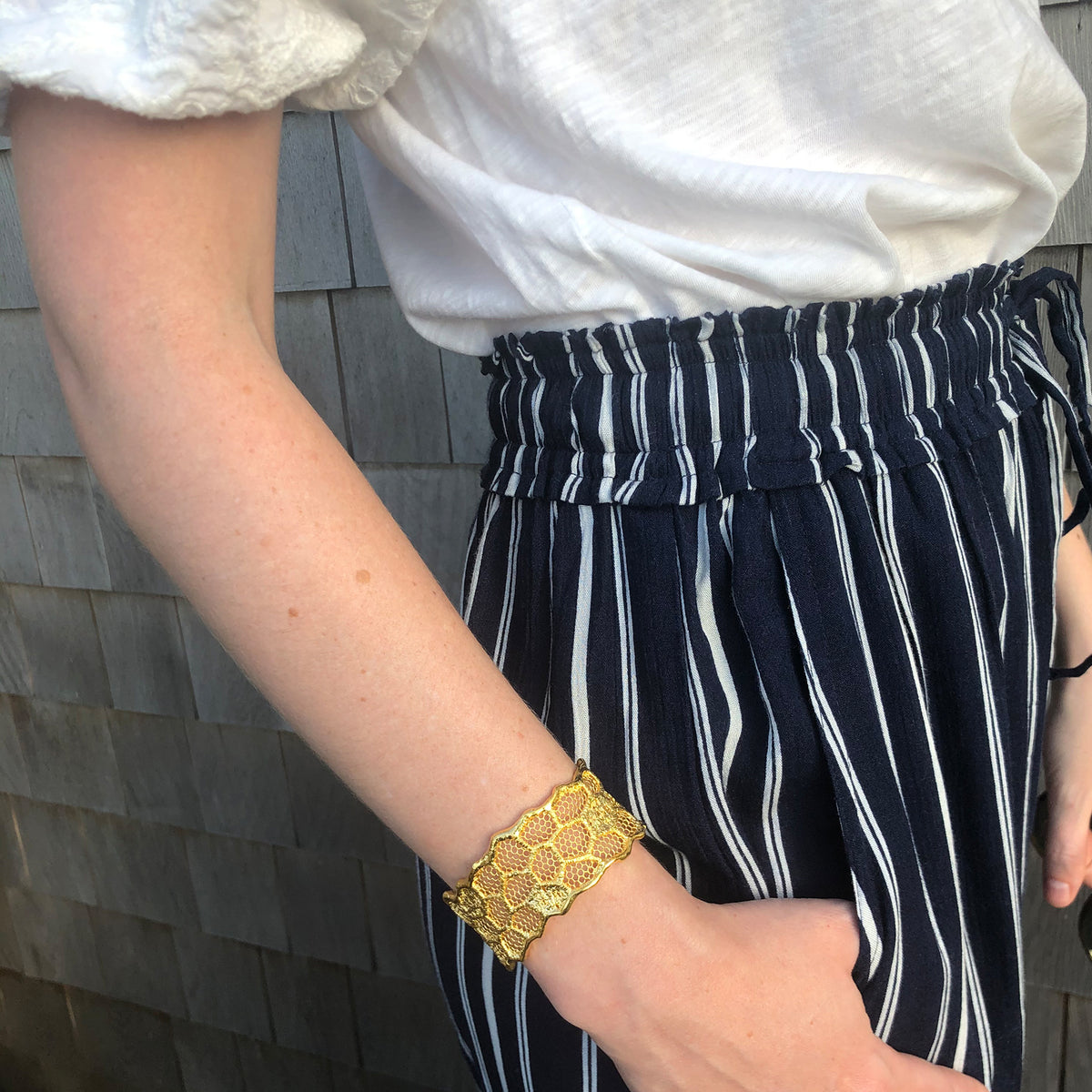 Model wearing a cuff bracelet made from an intricate honeycomb lace dipped in 24k gold.