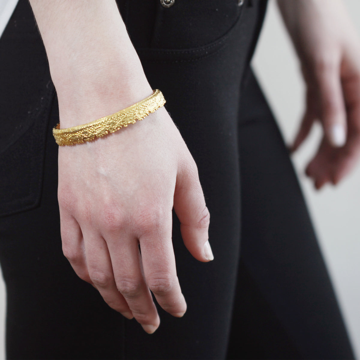Lace bangle bracelet in 24k gold worn by a model. Signed and numbered in the back.