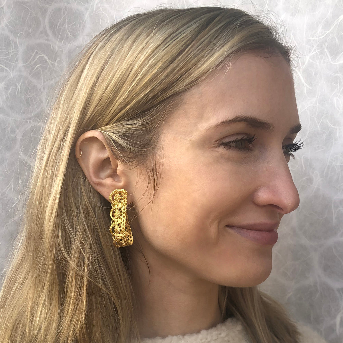 Model showing favorite earrings made from French 1920s lace forming a loop and solidified in 24k gold.