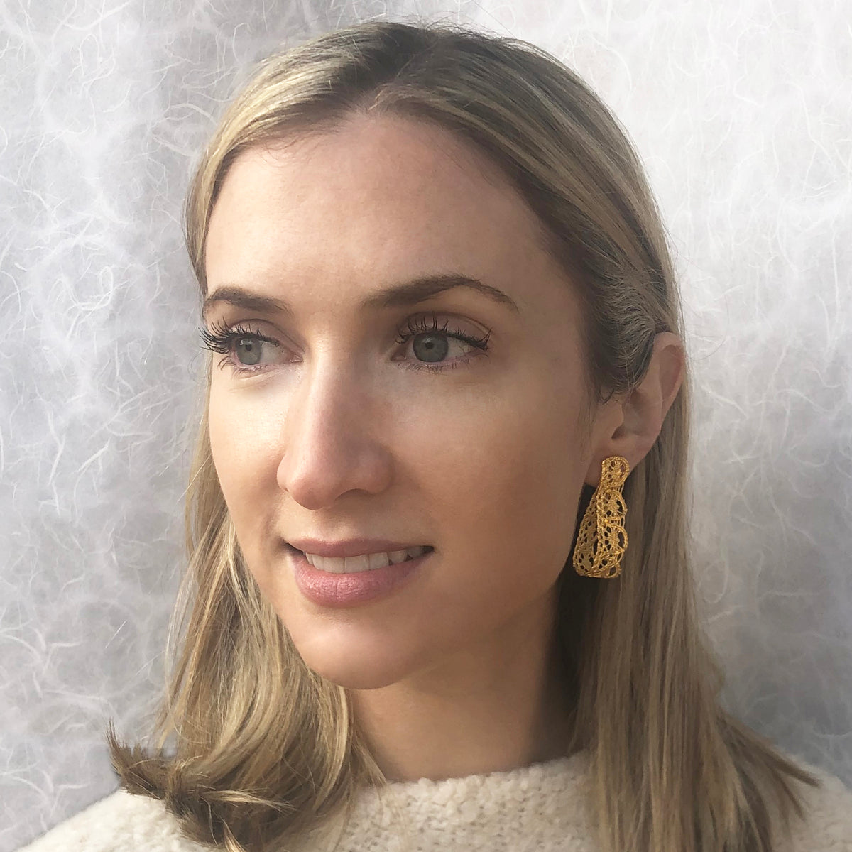 Model showing favorite earrings made from French 1920s lace forming a loop and solidified in 24k gold.