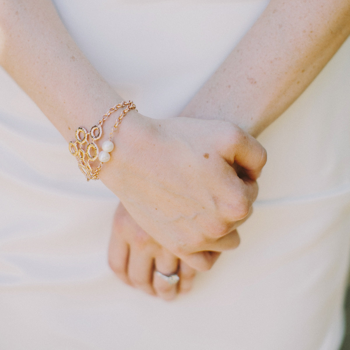 Exquisite chain bracelet with two pearls and a circular lace front dipped in rose gold on model.