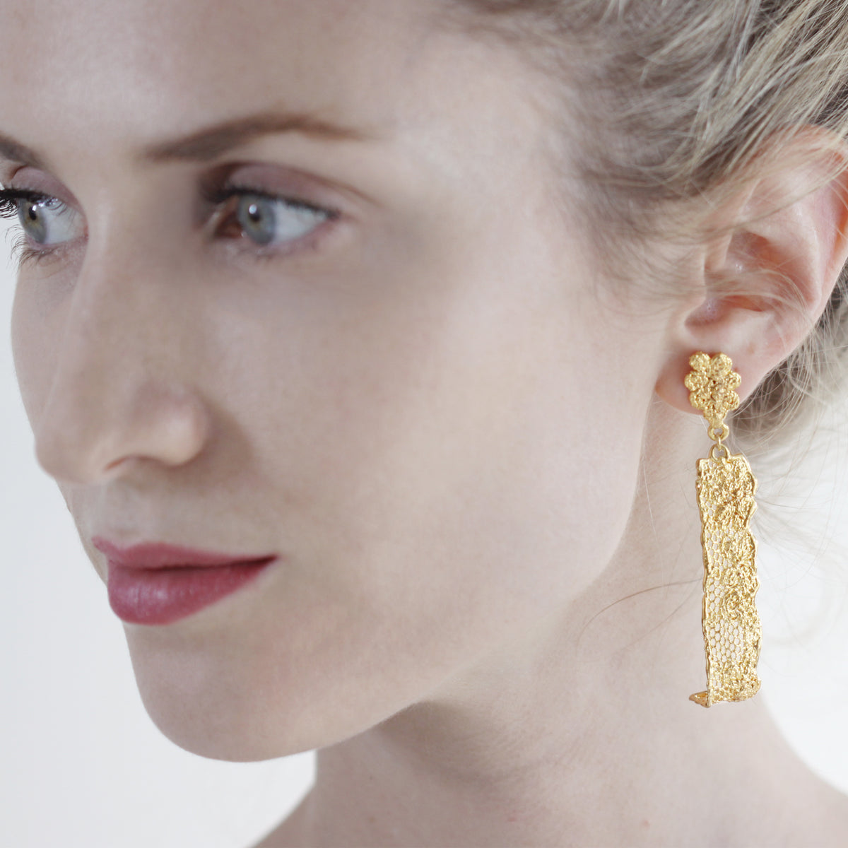 Long lace earrings with fine details in 24k gold worn by a model.