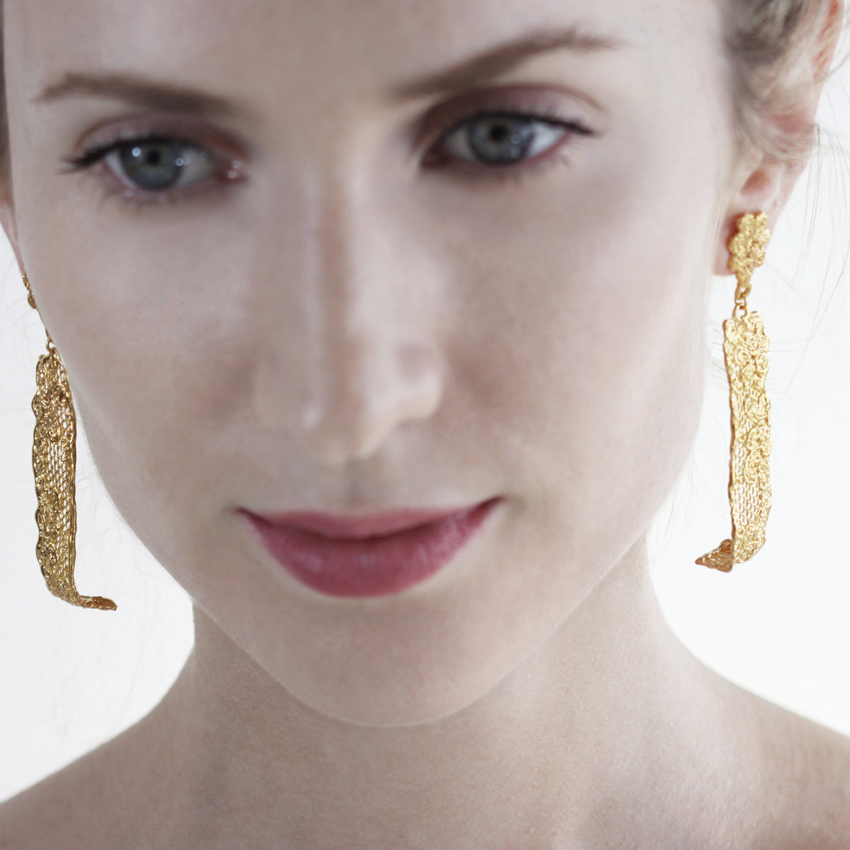 Long lace earrings with fine details in 24k gold worn by a model.