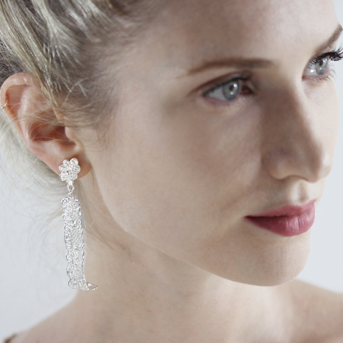 Long lace earrings with fine details in sterling silver worn by a model.