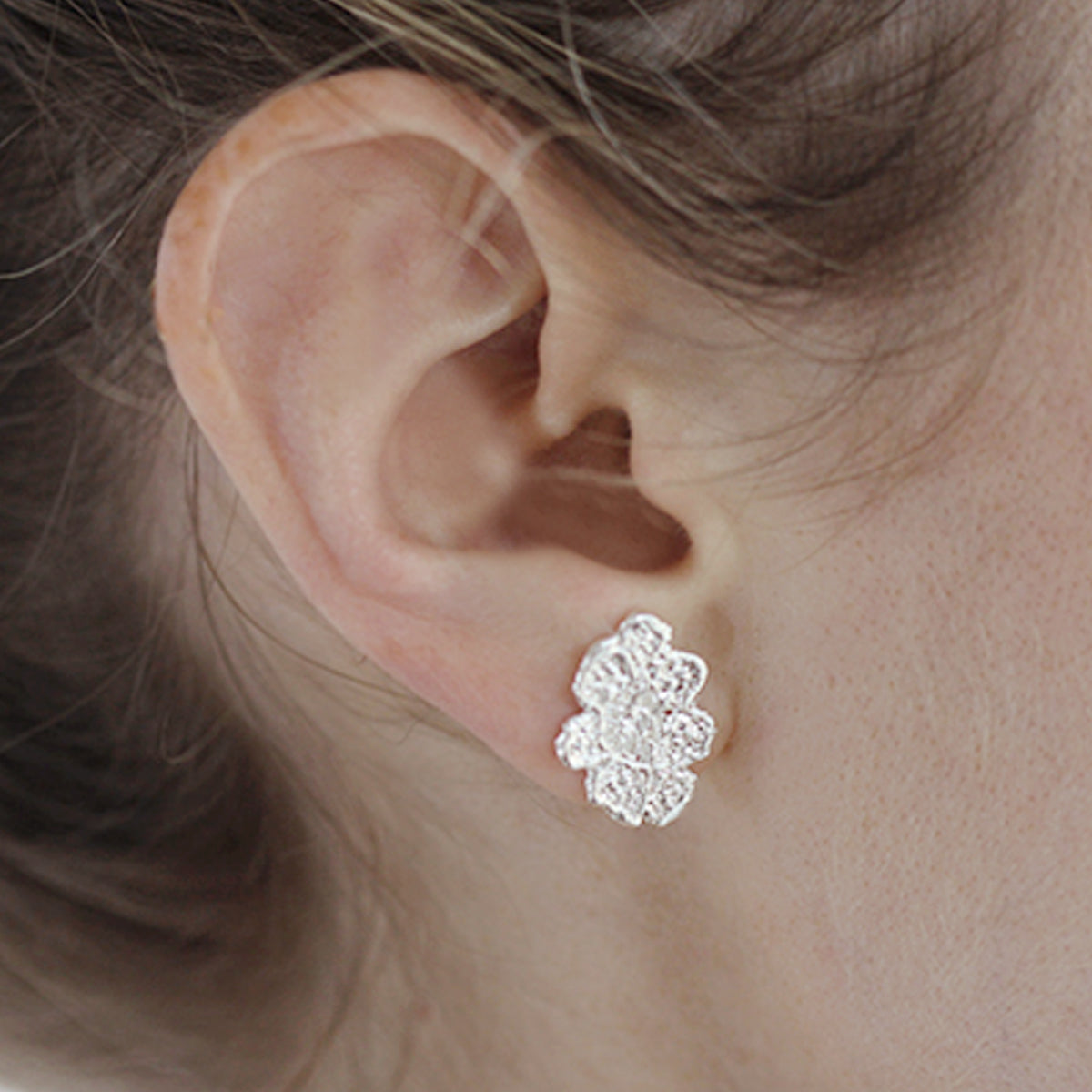 Small, exquisite stud earring in the shape of a lace flower dipped in sterling silver on model.