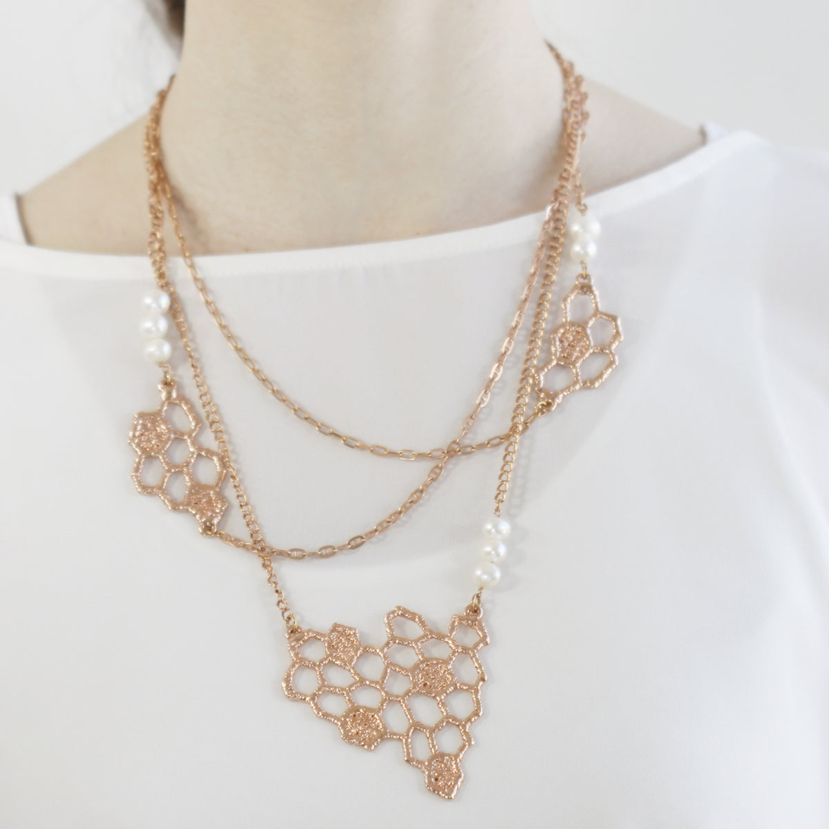 Honeycomb lace pendant necklace in rose cold with white fresh water pearls on a model.